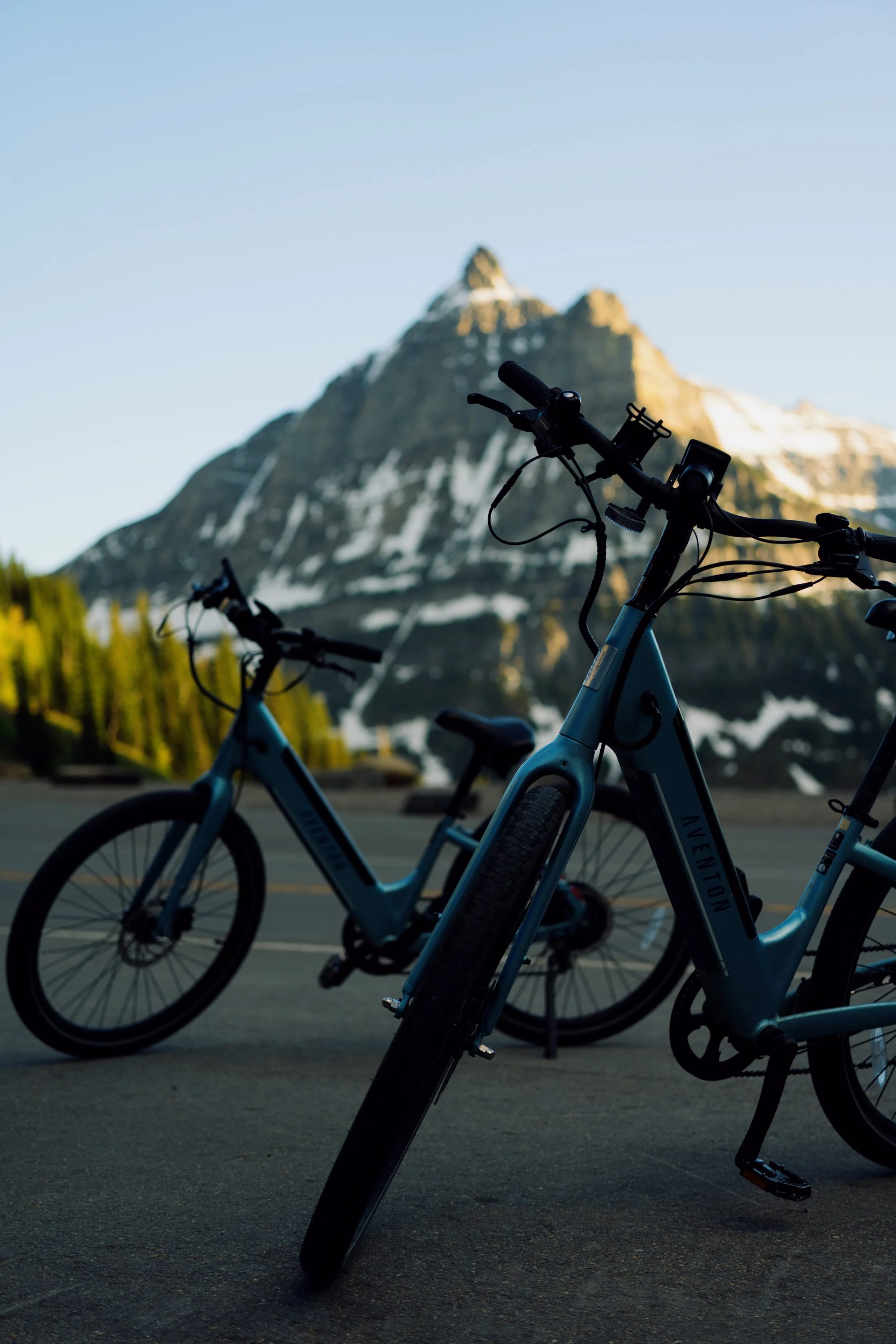 Two blue Aventon e-bikes parked with mountain peaks behind them