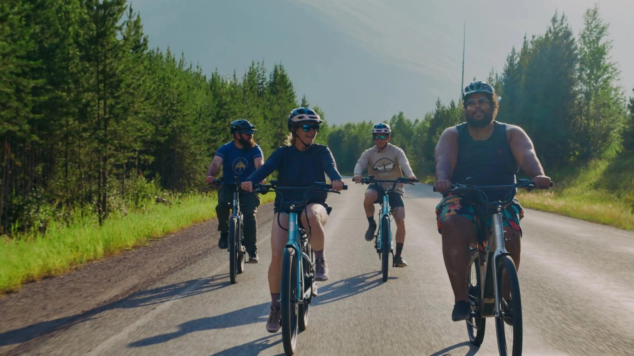 Four riders on e-bikes rolling down a quiet paved road
