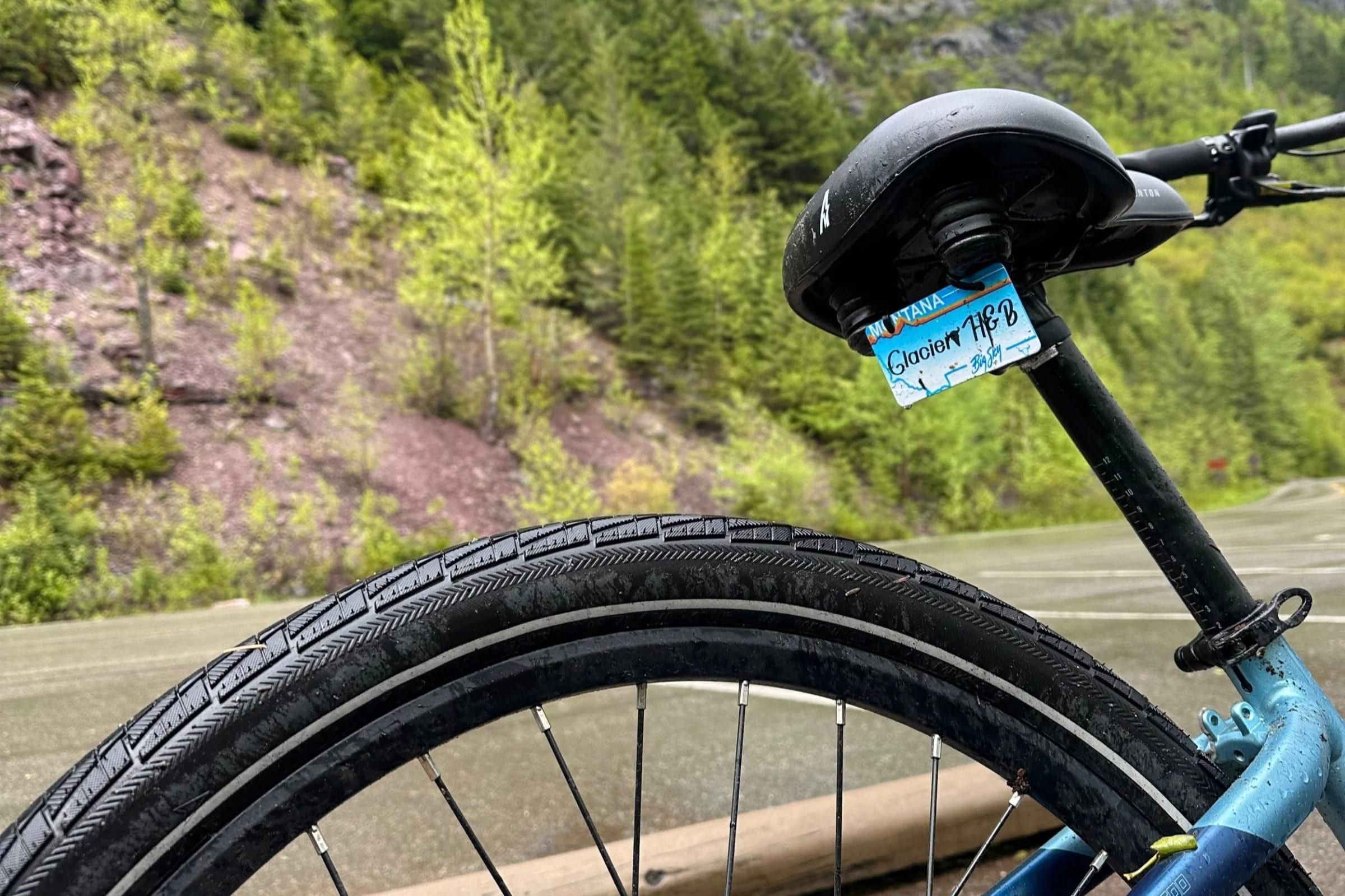 An e-bike's front wheel and handlebar on a wet road beside the forest