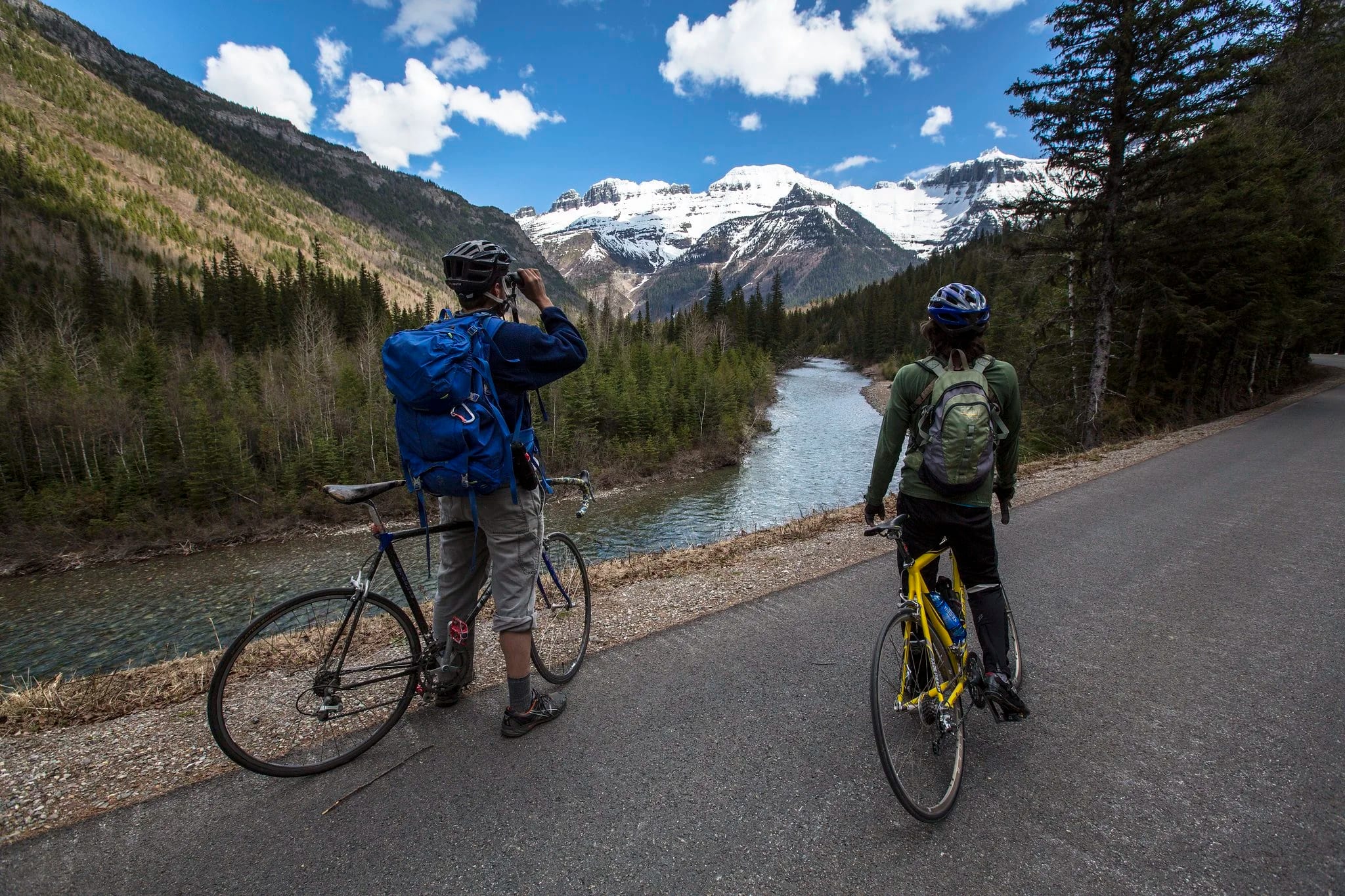 Two riders on a paved road with snowy peaks ahead