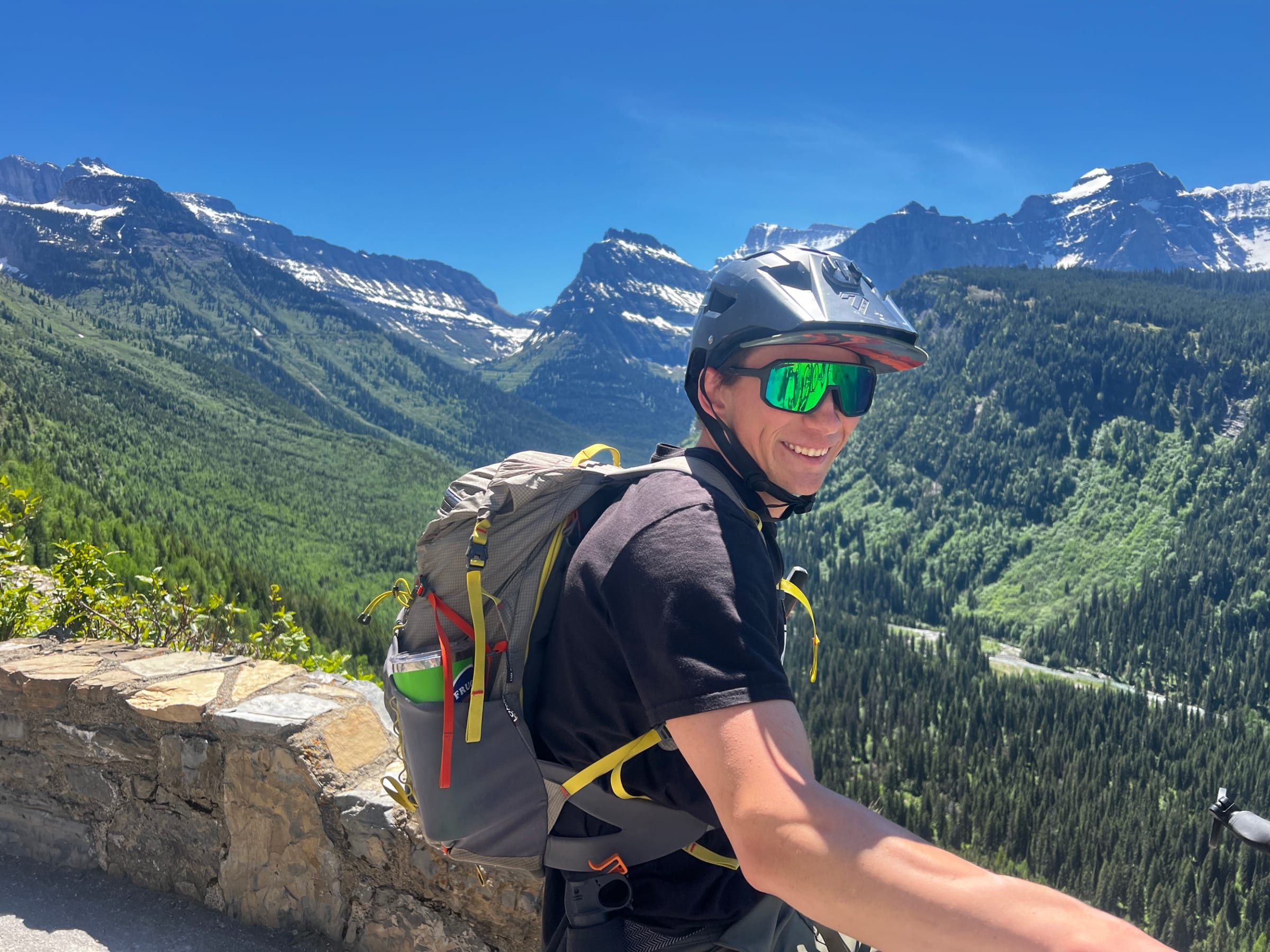 A rider with a backpack smiling on Going-to-the-Sun Road above the valley