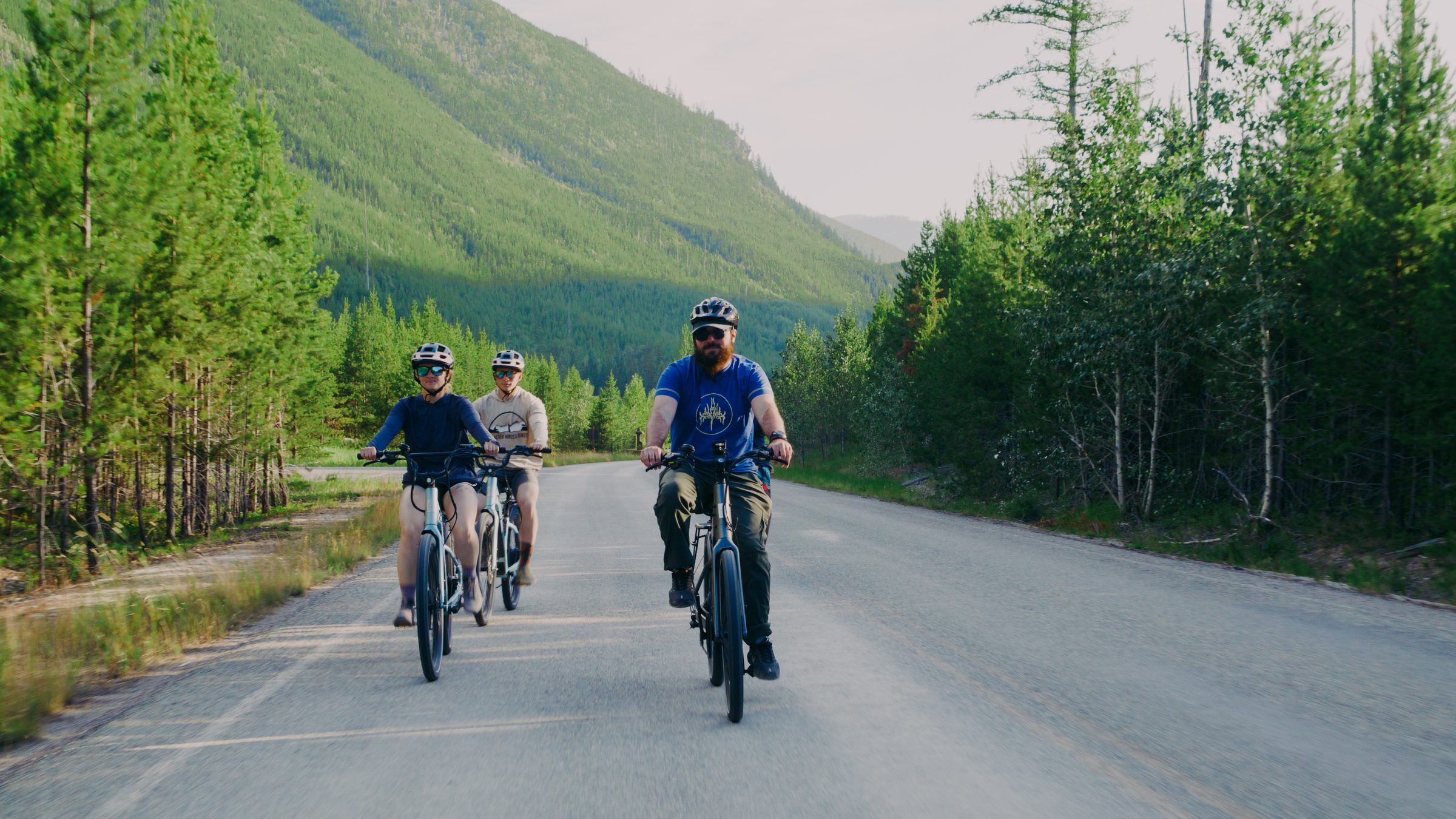 A small group riding e-bikes down a forest road toward the mountains